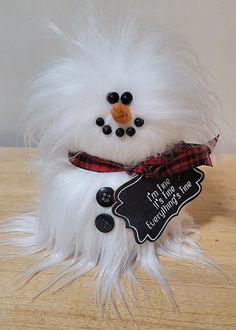 a white stuffed snowman with a red ribbon around its neck and black buttons on it's nose