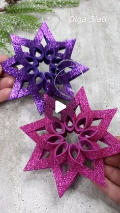 two purple and pink paper snowflakes are being held by someone's hands