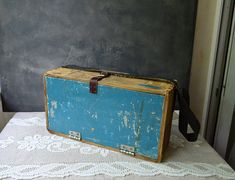 an old blue suitcase sitting on top of a white doily covered tablecloth next to a gray wall