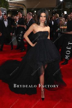 a woman in a black dress standing on a red carpet with people around her at an event