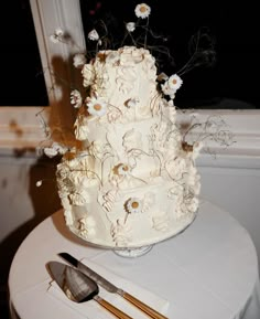 a white wedding cake sitting on top of a table next to a knife and fork