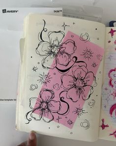 an open notebook with pink and black designs on it, next to a hand holding a pen