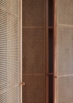 an open wooden cabinet sitting next to a wall with perfored panels on it