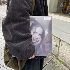 a person holding up a cd with a woman's face on it in front of a building