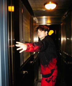 a young man in red pants and black shirt reaching for something on the wall with his hand