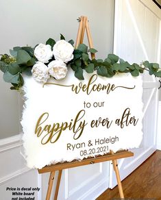 a welcome sign with flowers on it in front of a white wall and wooden easel