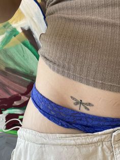 a woman's stomach with a small dragonfly tattoo on her side ribcage