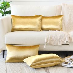 two gold pillows sitting on top of a white couch next to a pillow case and chair