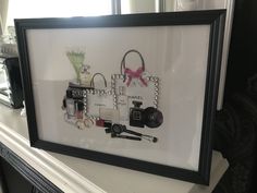 a black framed picture with cosmetics and other items in it on a mantle next to a window