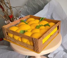 a wooden box filled with lemons on top of a white cake plate and covered in wax paper