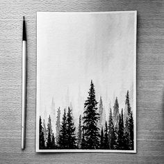 black and white photograph of pine trees on paper with pencil next to it, in front of a wooden table