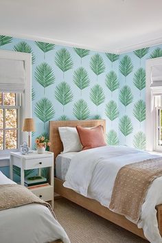 two beds in a bedroom with blue wallpaper and palm leaves on the wall behind them