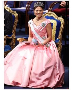 a woman in a pink dress and tiara sitting on a blue chair with red flowers