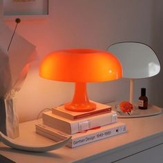 an orange lamp sitting on top of a white table next to books and a vase