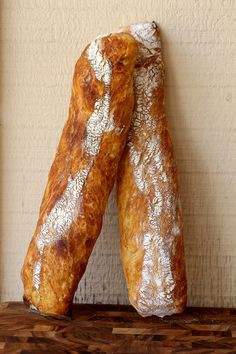 two loaves of bread sitting on top of a wooden table next to a wall