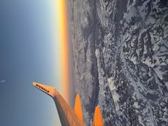 the wing of an airplane as it flies over a mountain range with a rainbow in the sky