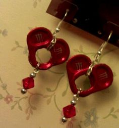 two red heart shaped earrings with beads hanging from the hooks on a wall next to a mirror