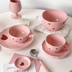 pink dishes and cups on a white table with hearts drawn on the plates, spoons and utensils