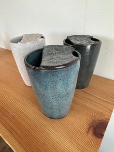 three ceramic vases sitting on top of a wooden table next to each other,