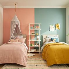 two beds in a bedroom with pink, blue and yellow walls on the wall behind them