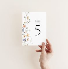 a person holding up a card with the number five printed on it and flowers all around