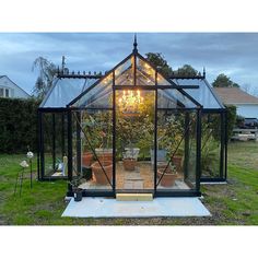 a small greenhouse with potted plants and lights in the front door area, surrounded by green grass