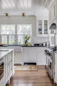 a kitchen with white cabinets and wood flooring next to a window covered in shutters