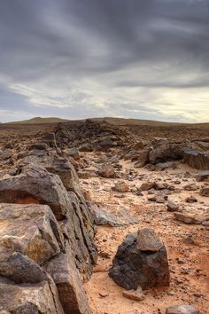 some rocks in the middle of a desert with dark clouds above them and dirt ground below