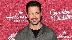 a man with a mustache standing in front of a red carpeted wall and smiling