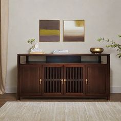 a living room with a rug and two paintings on the wall next to a wooden cabinet