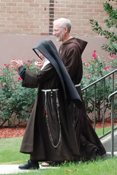 an older man dressed in robes and holding a book is walking down the sidewalk with his hands together