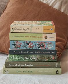 a stack of five books sitting on top of a bed next to a brown pillow