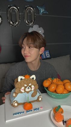 a boy sitting at a table with a teddy bear and oranges in front of him