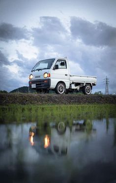 a white truck parked on top of a grass covered field next to a body of water