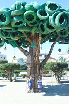 two children standing in front of a giant tree made out of old tire rims