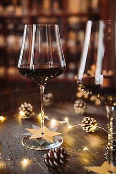 a glass of red wine sitting on top of a wooden table next to pine cones