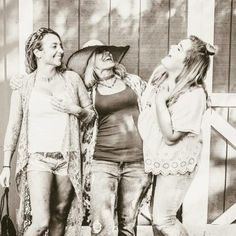 three women standing next to each other in front of a barn