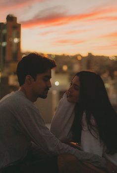 a man and woman sitting next to each other on top of a building at sunset