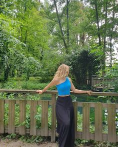 a woman in a blue top is standing on a wooden fence and looking at the woods