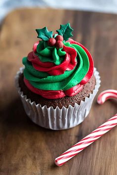 a cupcake with green and red frosting next to a candy cane on a wooden surface