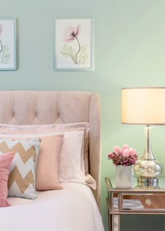 a bed with pink and white pillows on top of it next to a table with flowers