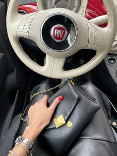 a woman's hand on the steering wheel of a car holding a black purse