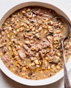 a white bowl filled with beans and meat next to a spoon on top of a table