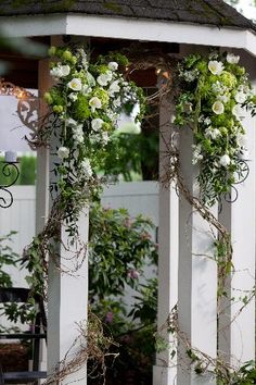 an outdoor gazebo decorated with white flowers and greenery