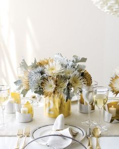 a table set with white and gold plates, silverware and flowers in vases