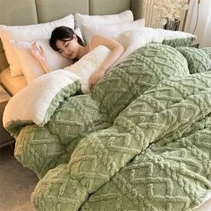 a woman laying on top of a bed covered in green blankets and pillows with white pillows