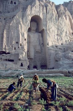 some people are working in the field near a large statue