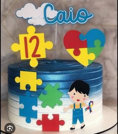 a birthday cake decorated with puzzle pieces and a little boy holding a heart on top