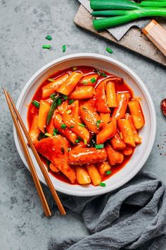 a white bowl filled with carrots covered in sauce and chopsticks next to it