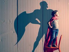 a young boy standing on top of a red chair next to a shadow of a man